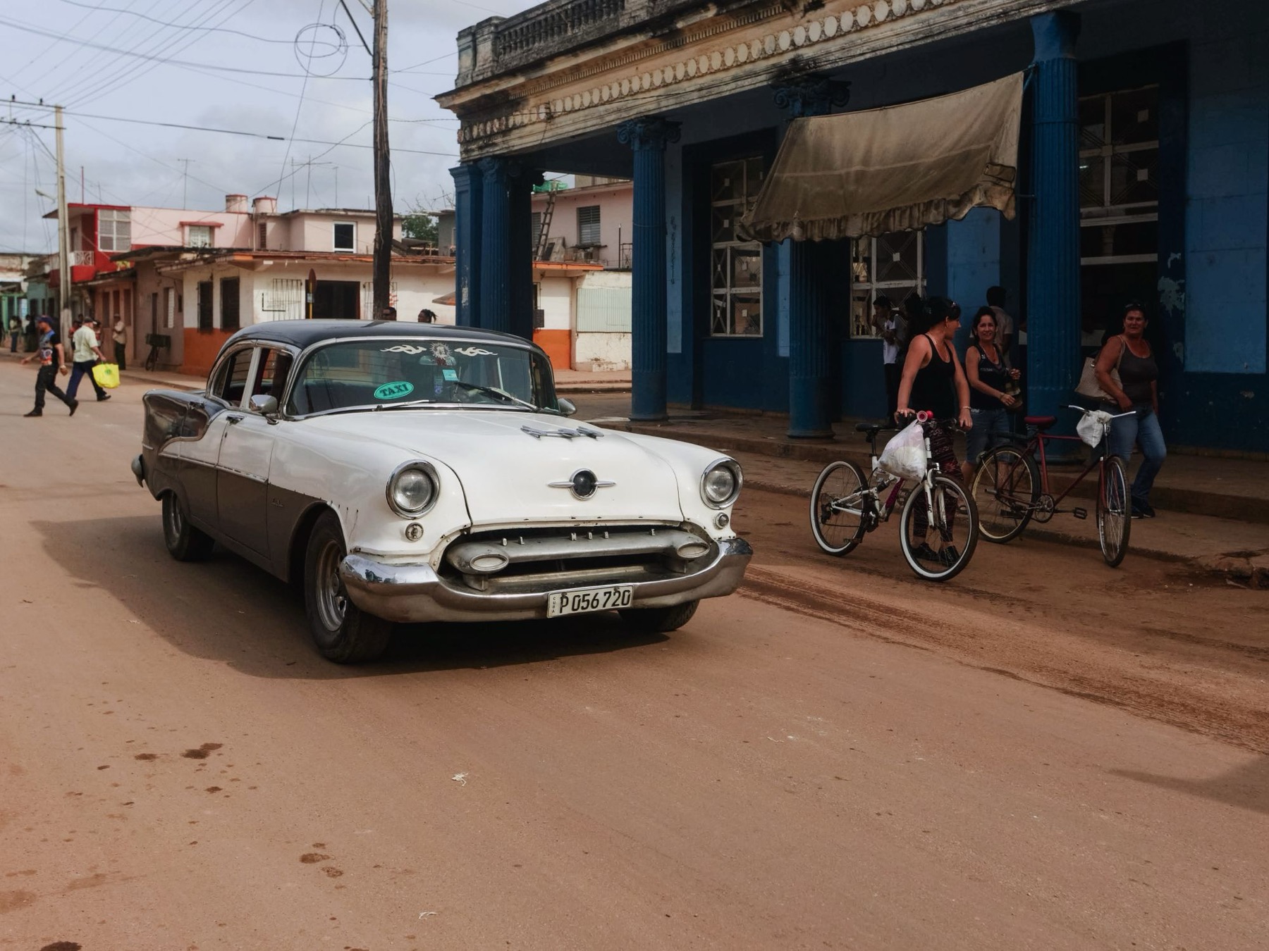 A vintage car and neighbors on the street outside the restaurant
